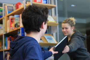 Schülerin überreicht Schüler ein Buch in Bibliothek